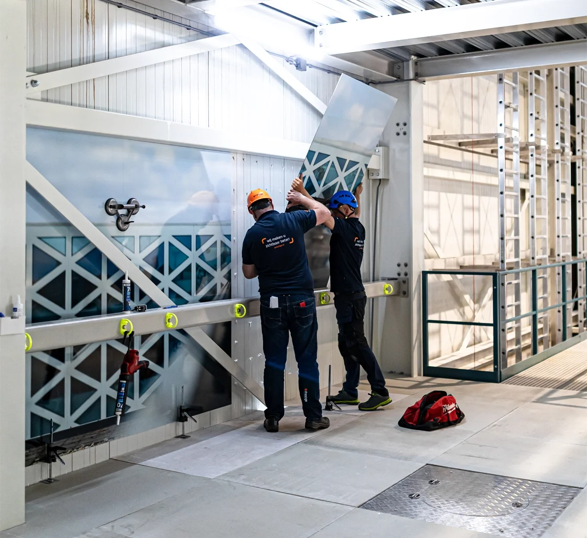 Projectsign Prestige Reclame 13 Twee monteurs van Prestige Reclame monteren een groot fotopaneel op de wand van een bedrijfshal.